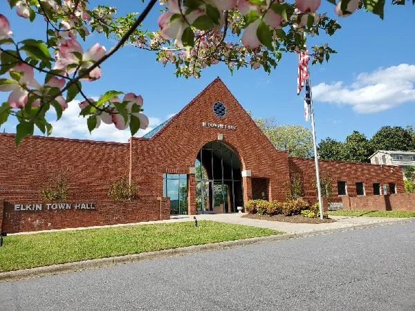 Elkin Town Hall, a one-story brick building with a tall arched entry, framed by flowering branches.