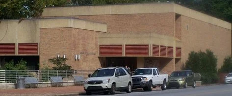 The Elkin Public Library, a one-story tan brick building with a parking lot in front.