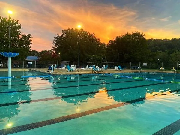 The Elkin Municipal Pool at sunset, lane lines on still water under an orange and blue sky.